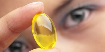A woman holding a yellow vitamin capsule
