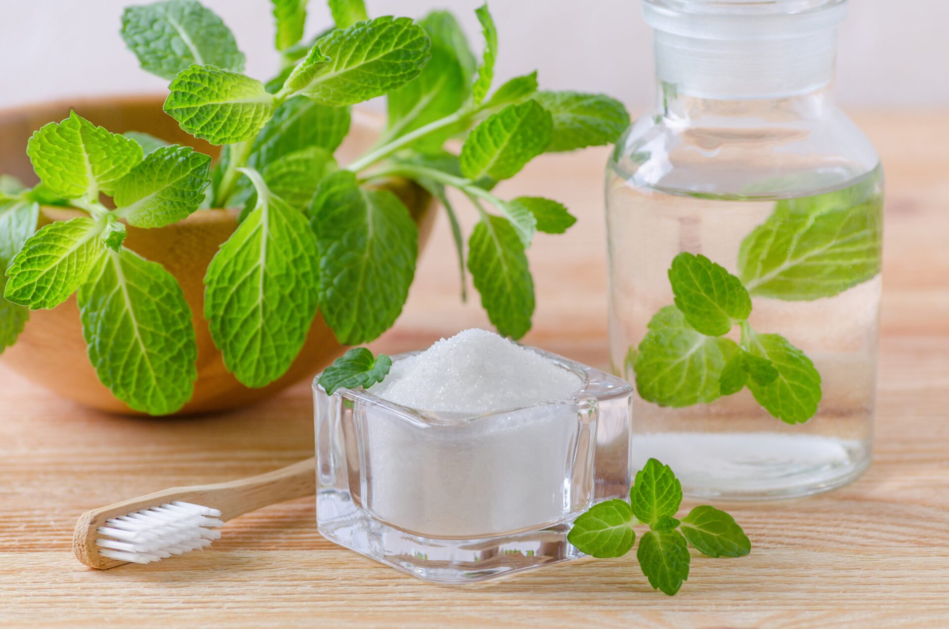 alternative natural mouthwash bottle with toothpaste xylitol, soda, salt, and wood toothbrush closeup, mint on wooden background