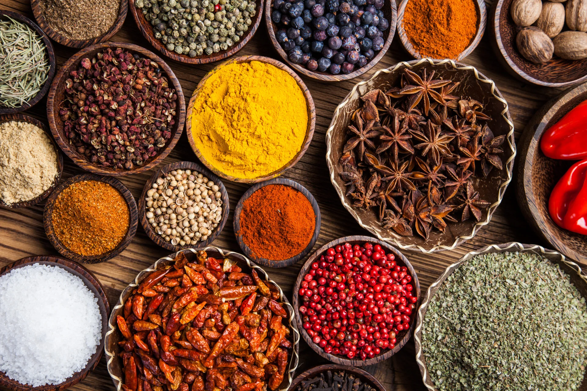A selection of various colorful spices on a wooden table in bowls