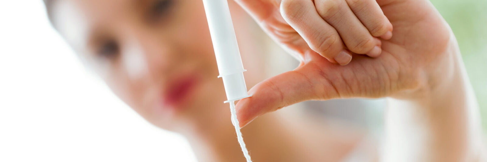 Shot of pretty young woman holding and looking tampon in the bathroom.
