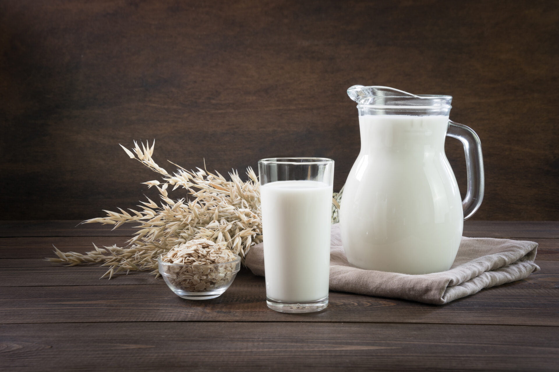 Fresh oat milk in glass and pitcher on dark wooden table. Healthy vegan eating. Rustic style.