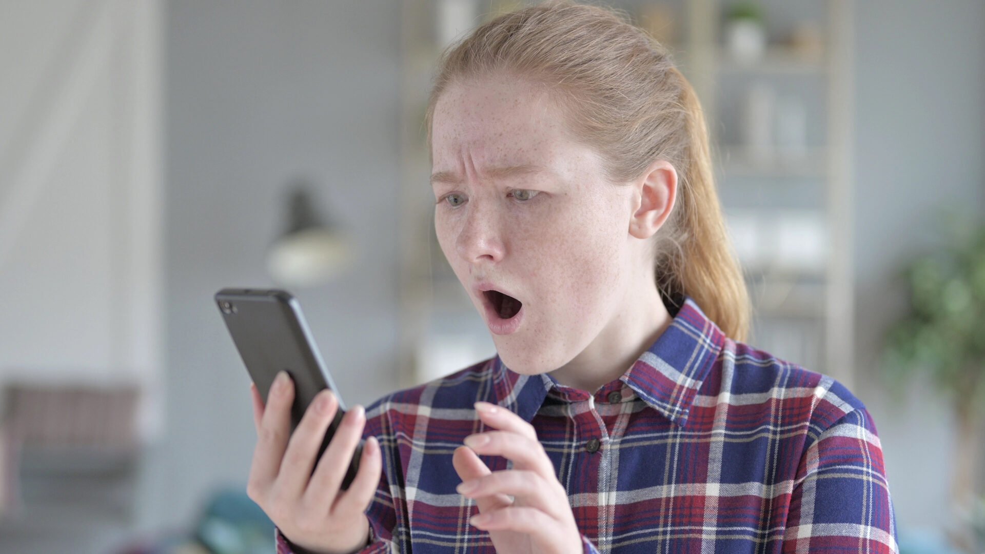 Young Woman Using Smartphone With Shocked Expression