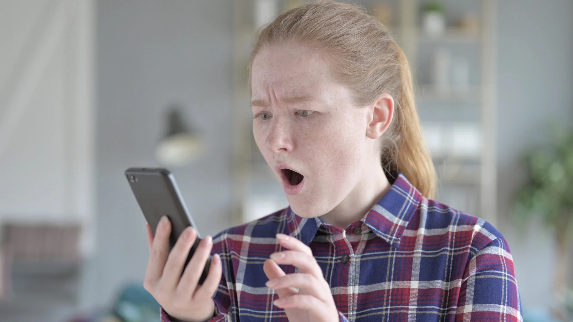 Young Woman Using Smartphone With Shocked Expression