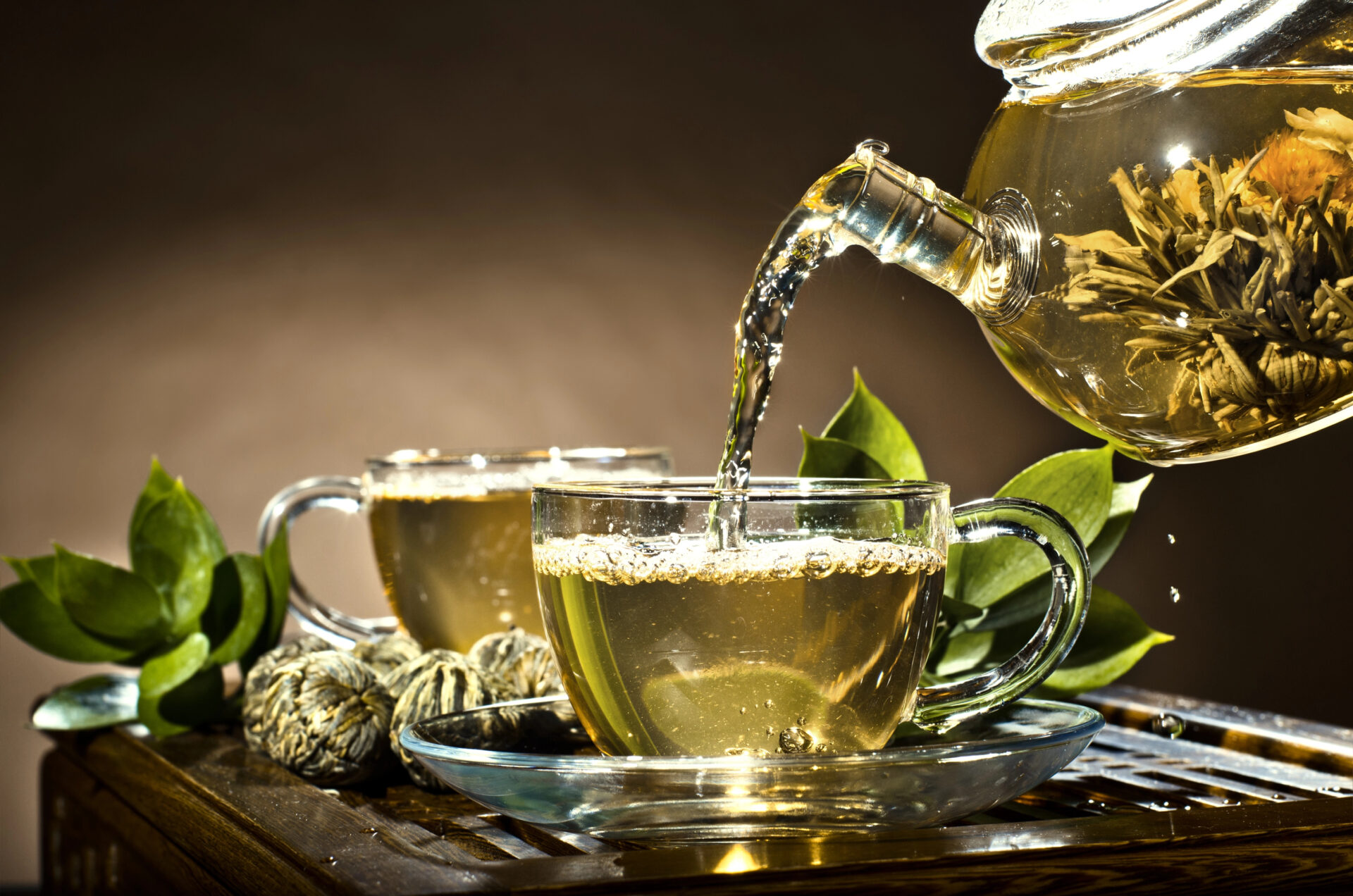 Green tea being poured on the table to a glass tea cup