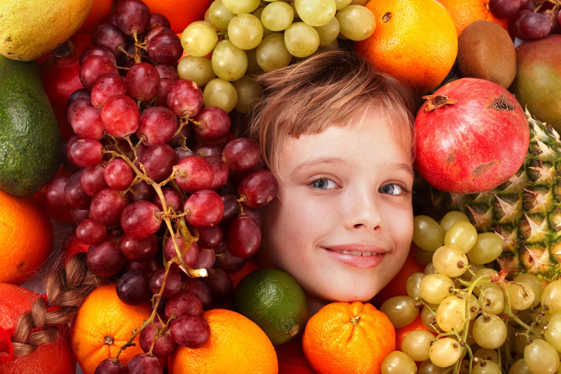 child laying within fruits like grapes, oranges, etc