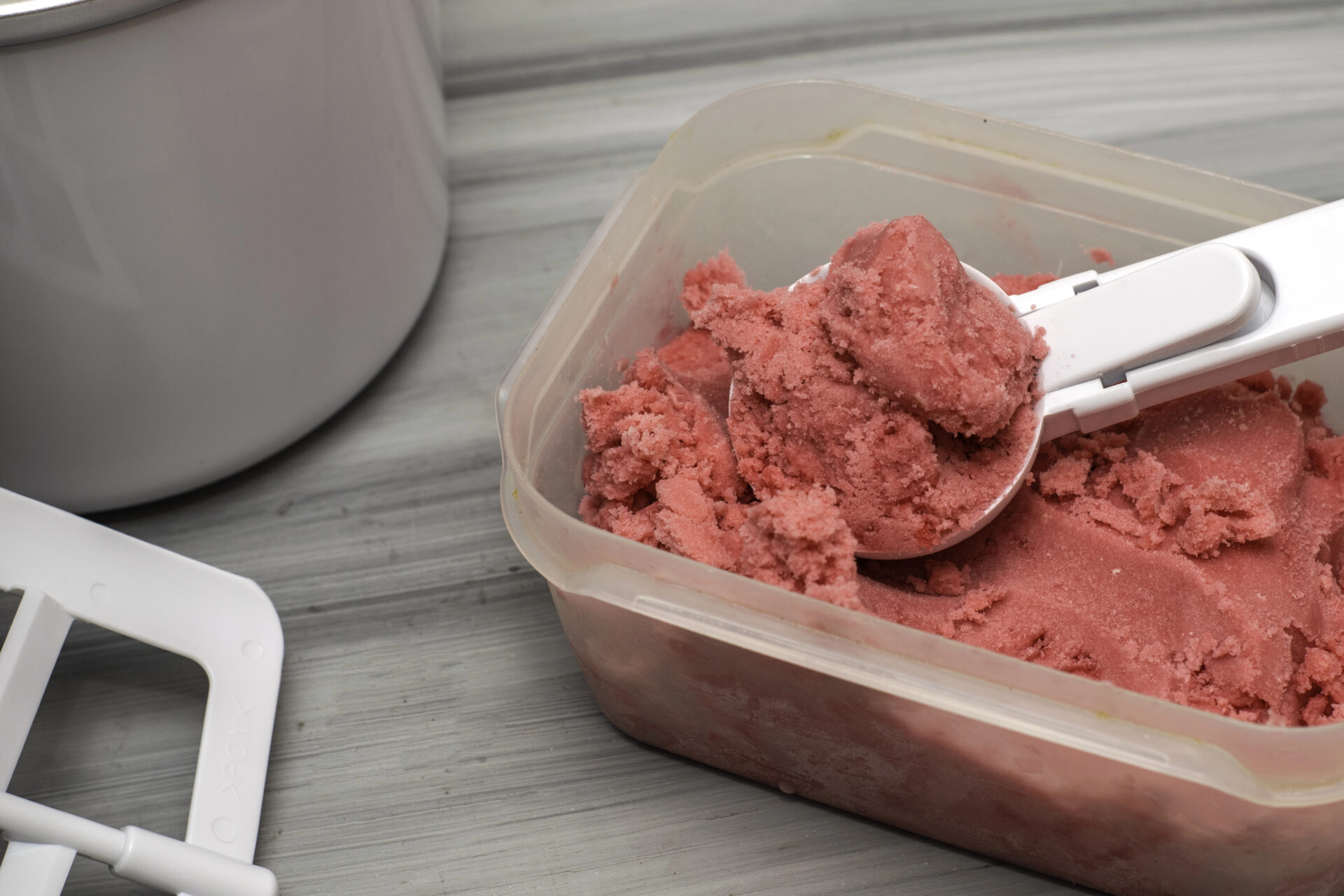 Raspberry ice cream sitting on the table in a plastic canister