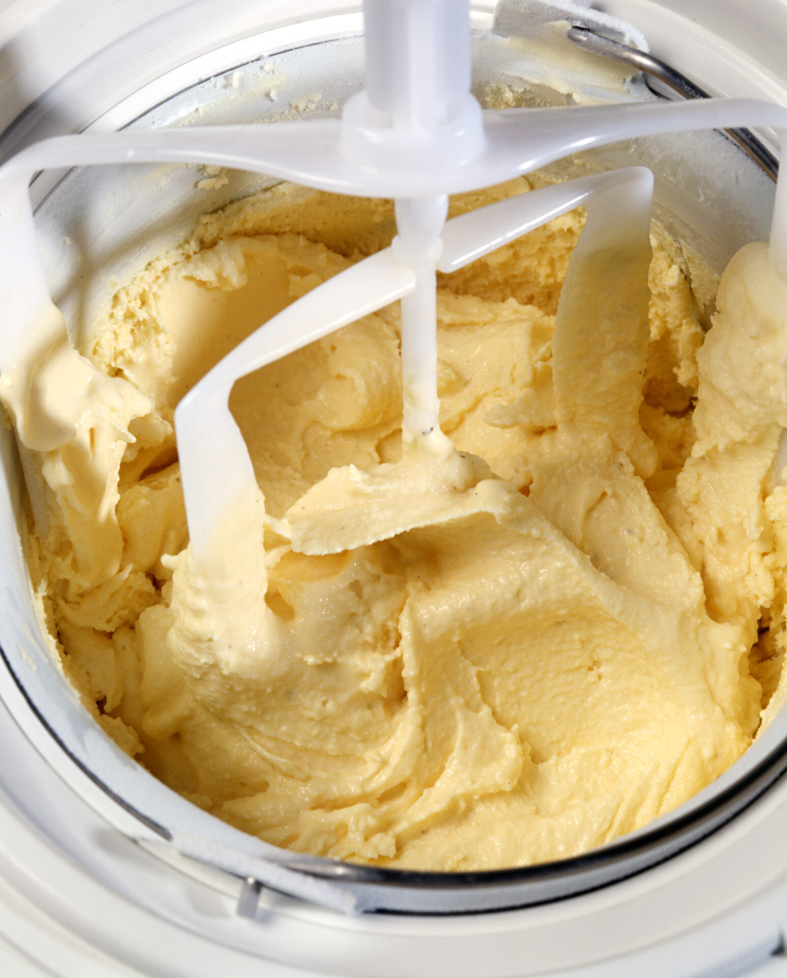 Overhead view looking into a stainless steel mixing bowl of the whisk and blender on an icecream making machine during preparation of handmade gourmet Italian ice cream