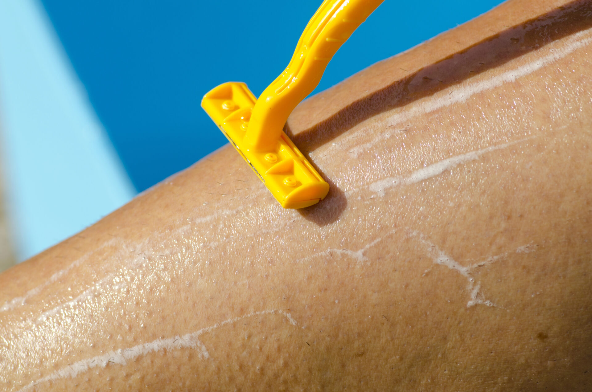 Woman shaving her legs with a yellow razor coated in PFAS