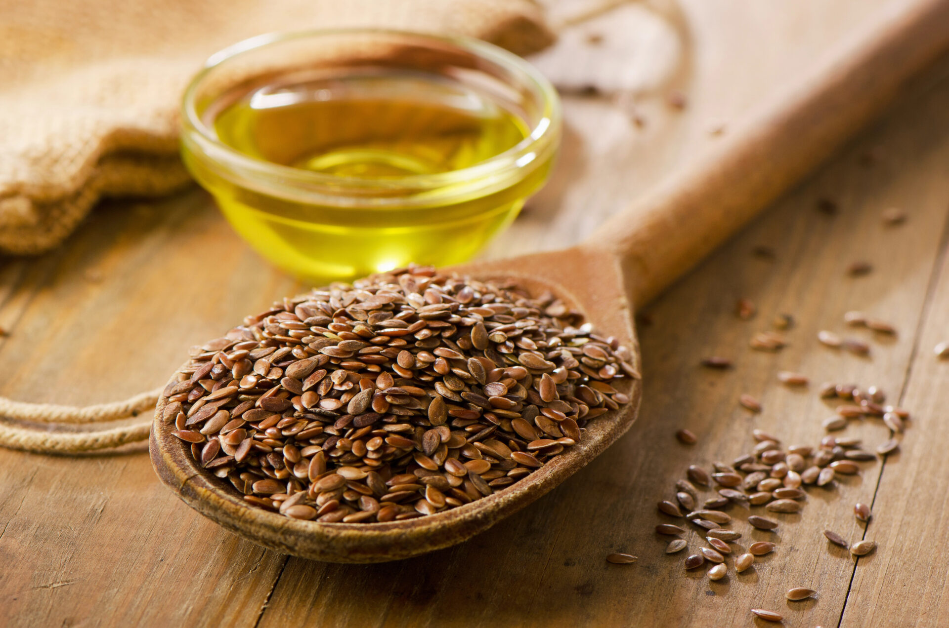 Flaxseed sitting in a wooden spoon with some flaxseed oil on a tiny bowl on the table