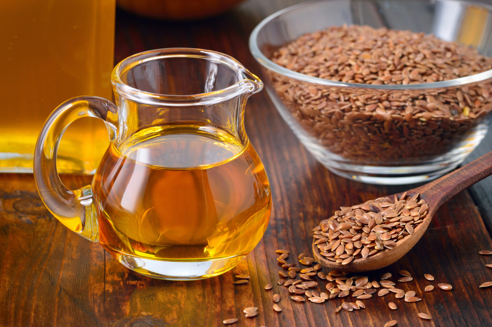 Flaxseed oil sitting next to a glass bowl of flaxseeds
