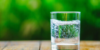 A glass of water on green background. The wooden table. Pure water with gas. Sparkling water tested for PFAS "forever chemicals."