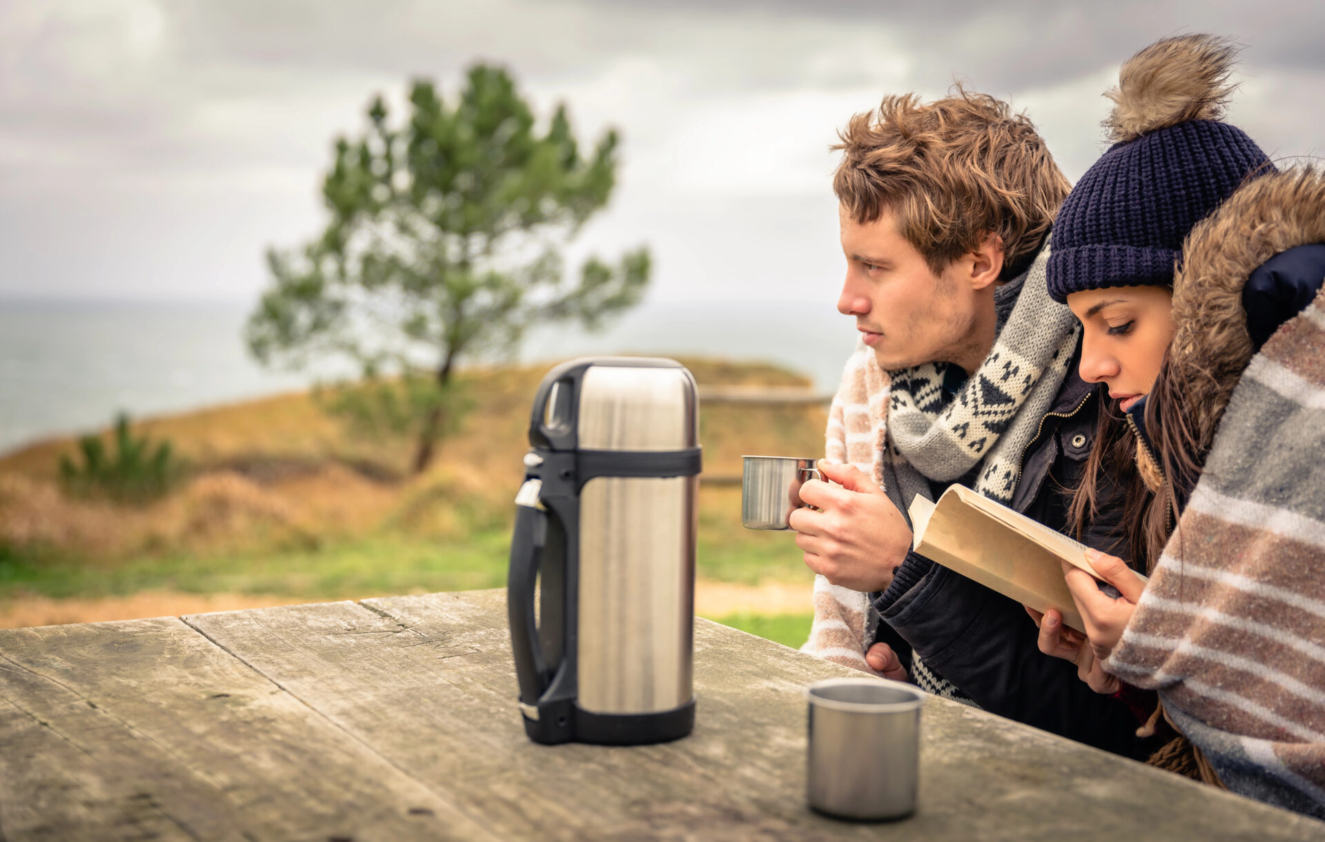 Couple sitting in the park in the cold drinking coffee from a hot beverage container