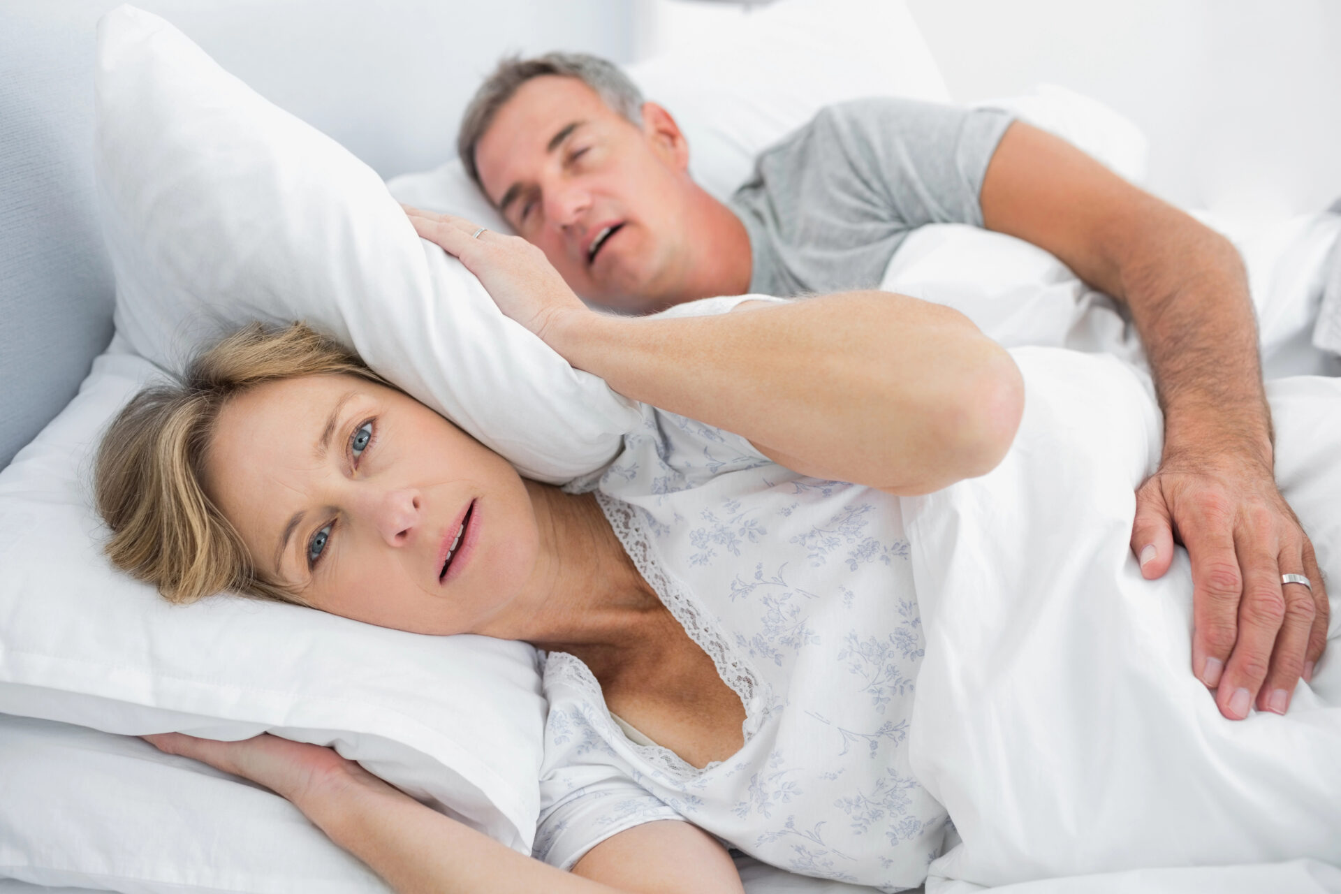 Woman covers ears in pillow as husband snores