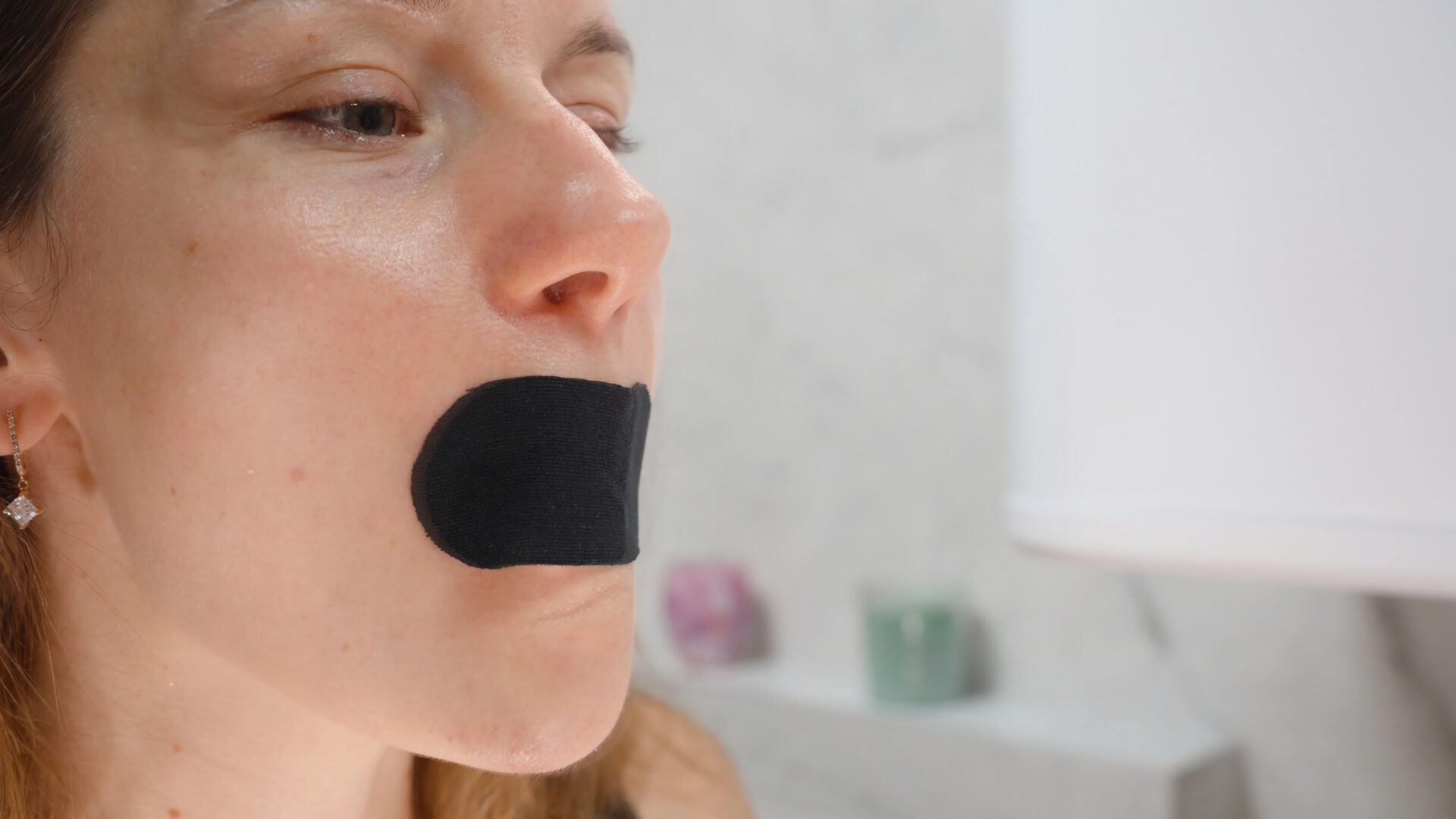 Woman wearing mouth tape in front of the bathroom mirror