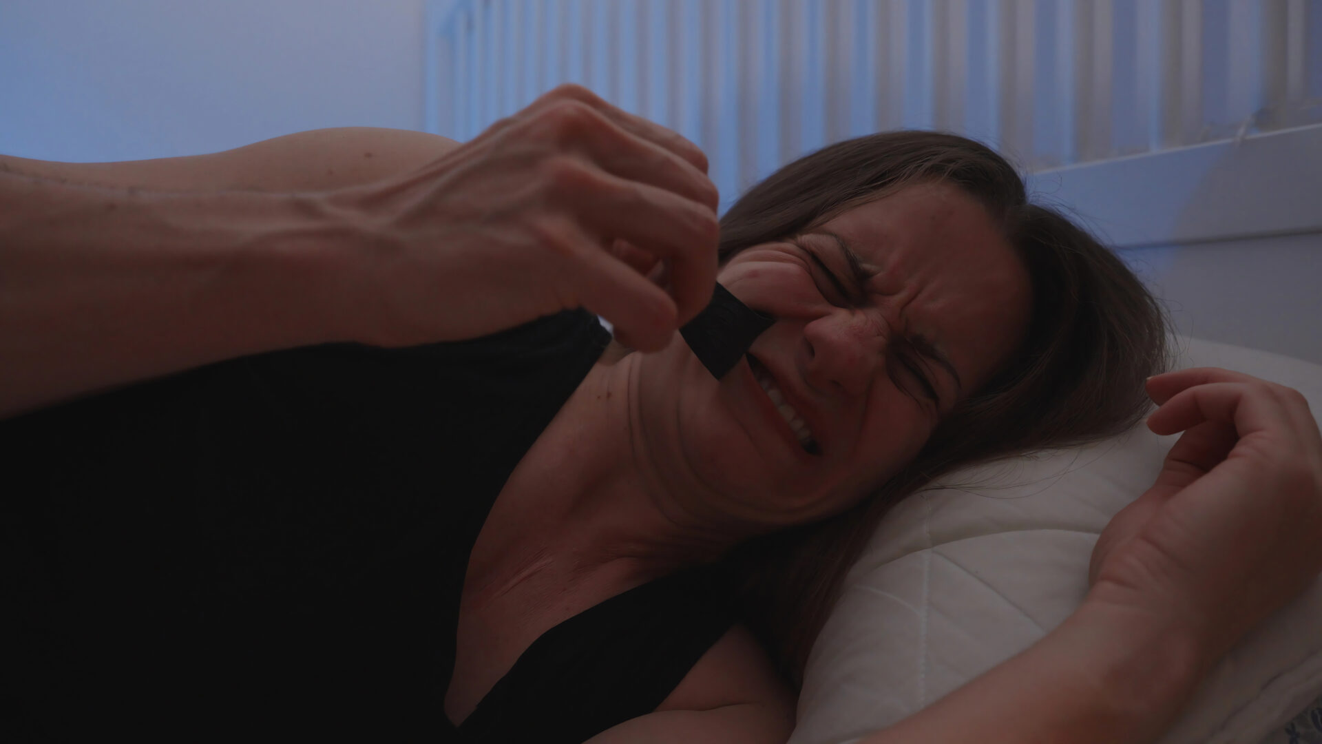 Woman ripping mouth tape off her mouth in the morning in bed