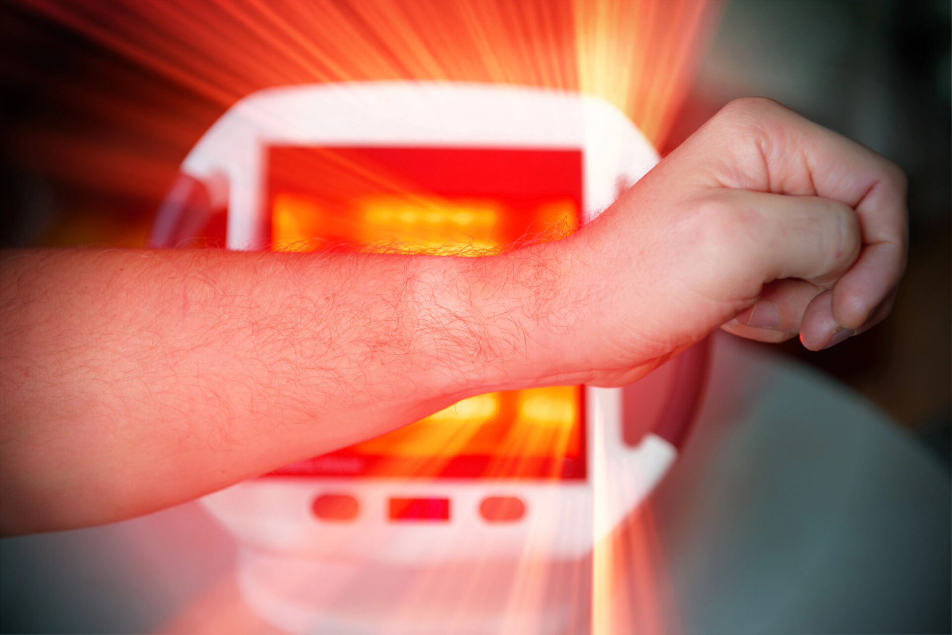 Man treating pain in the hand with infrared light therapy. The man sits at the table near the healing lamp.