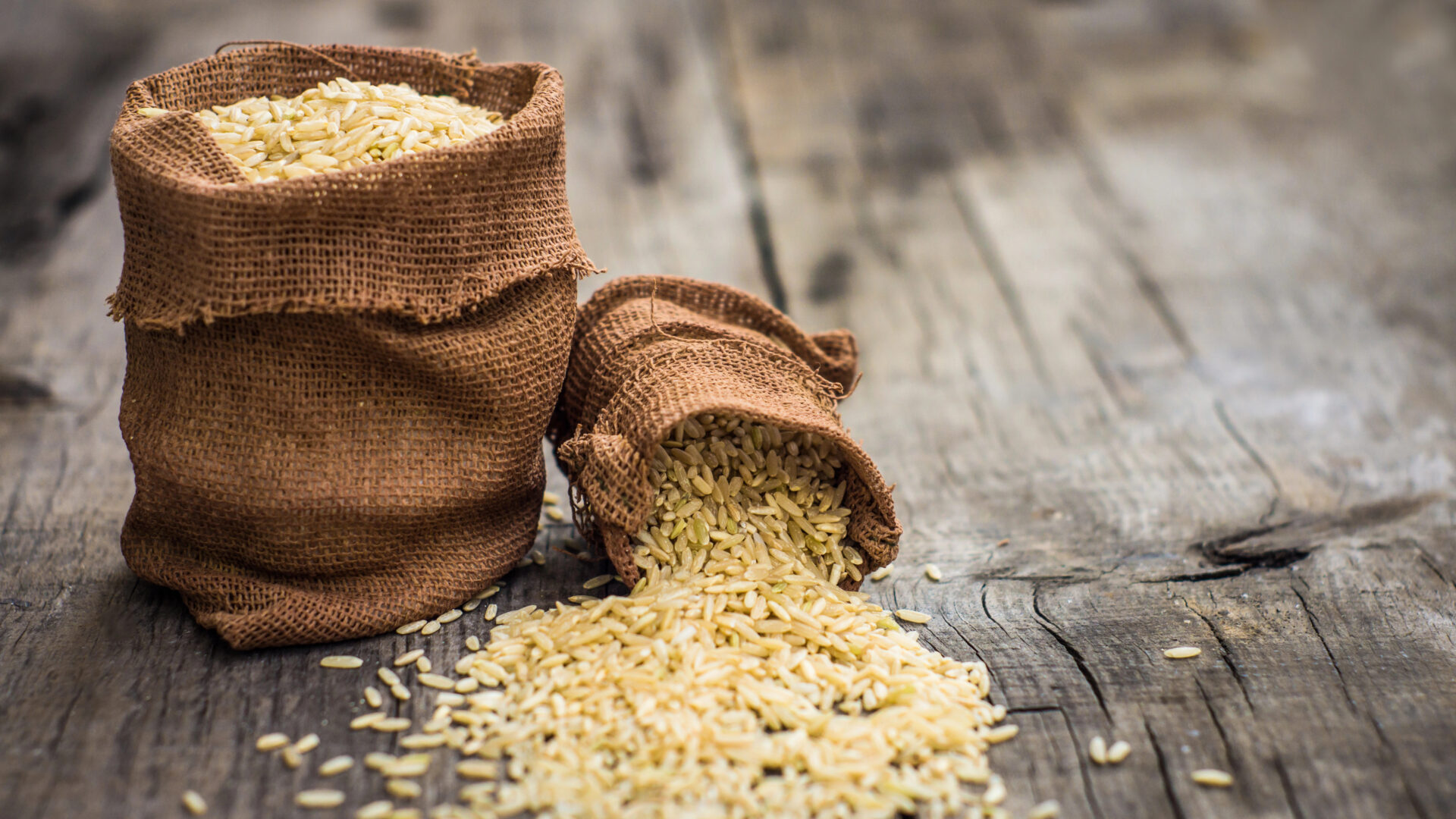 Small bags with brown rice on wooden background
