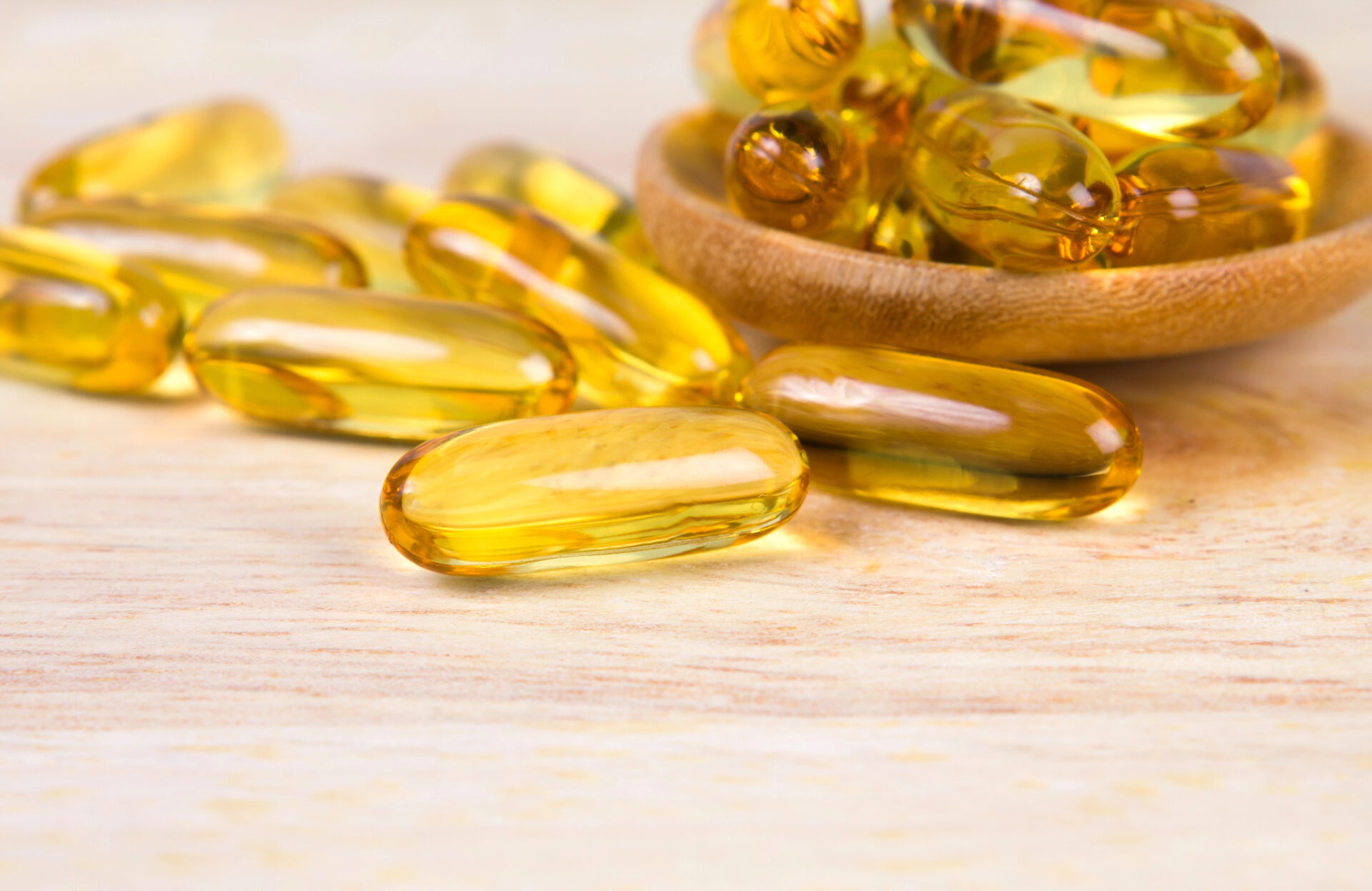 Closeup the yellow soft gelatin supplement fish oil capsule on wooden plate