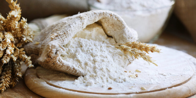 Flour in burlap bag on cutting board and wooden table background