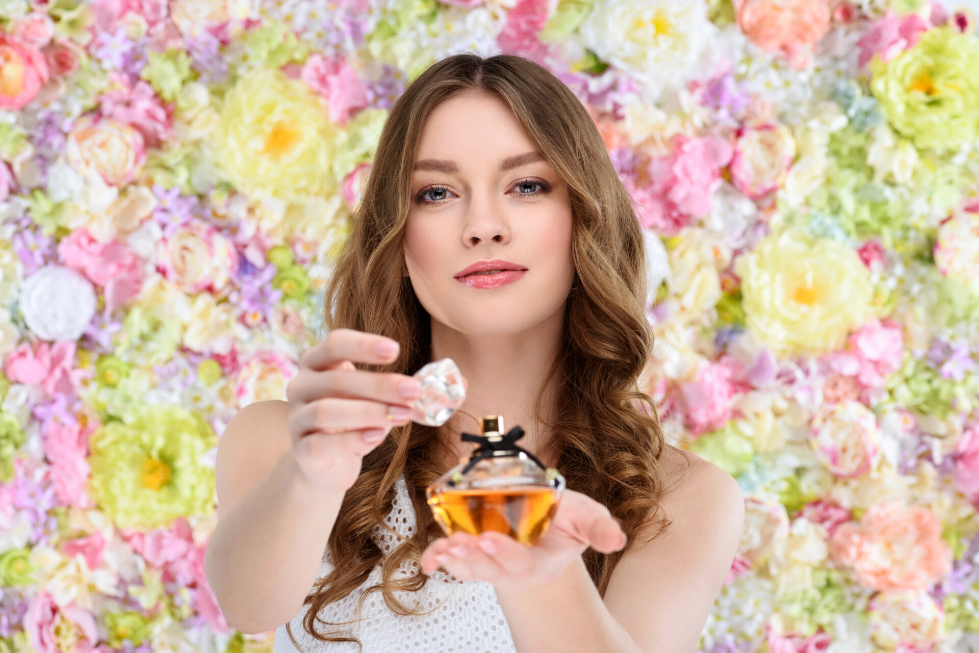 Woman standing next to flowers holding perfume in her hands