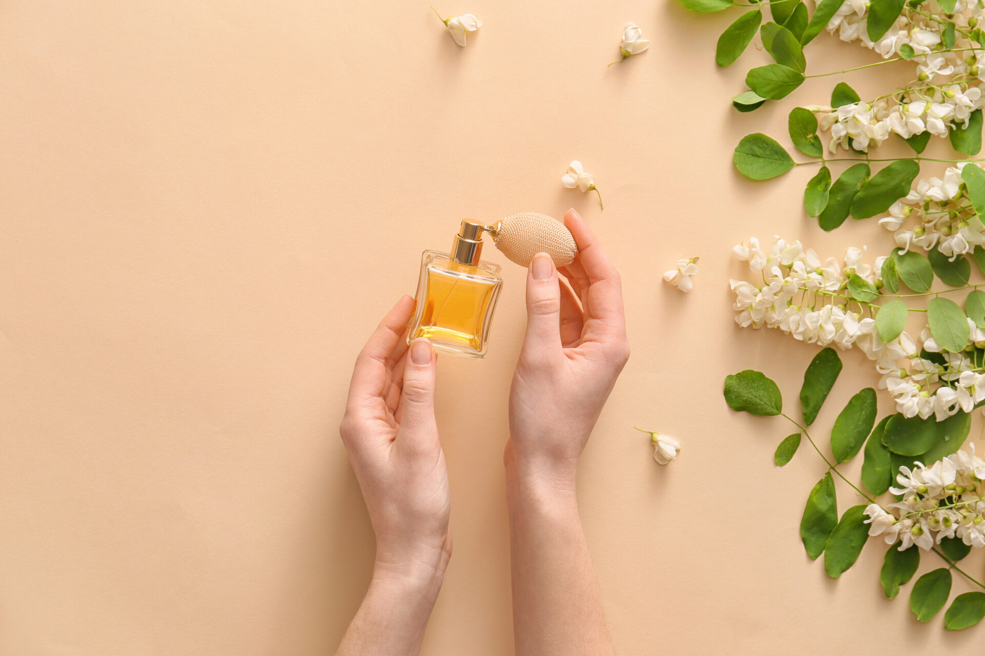 Female hands with perfume and flowers on color background