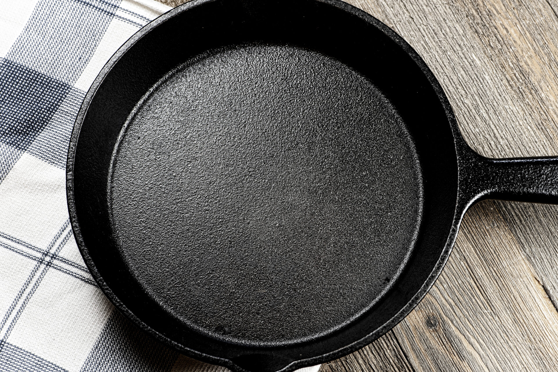 Large black cast iron cooking pan resting on kitchen towel and wooden table surface